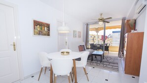 Ein Essbereich mit weißem Tisch und Stühlen, einem Deckenventilator und Blick auf den Außenbalkon.
