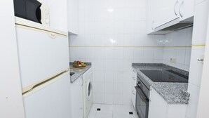 Eine kompakte Küche mit weißen Schränken, einer Waschmaschine, einer Mikrowelle und einer Arbeitsplatte aus Granit.