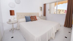 Ein Schlafzimmer mit einem großen Bett, einem Nachttisch mit Lampe und einem Fenster mit Vorhängen.