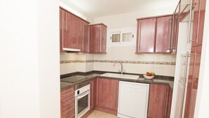 A compact kitchen with wooden cabinets, a dishwasher, a stove, and a sink. - A85 EDIFICIO OCEANIC 304 (Calpe)