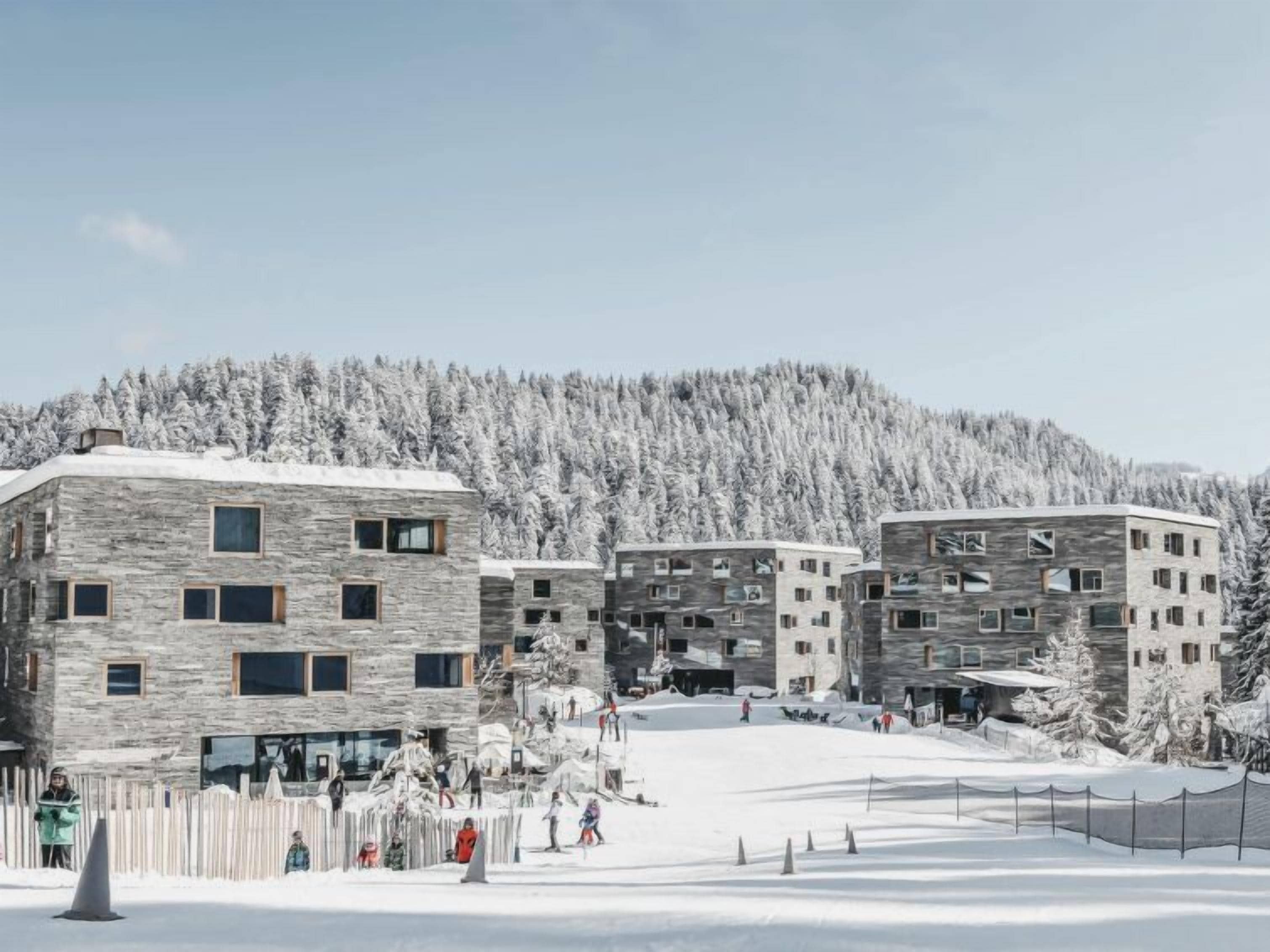 A modern building complex with multiple floors and large windows, surrounded by snow-covered trees and a clear sky.