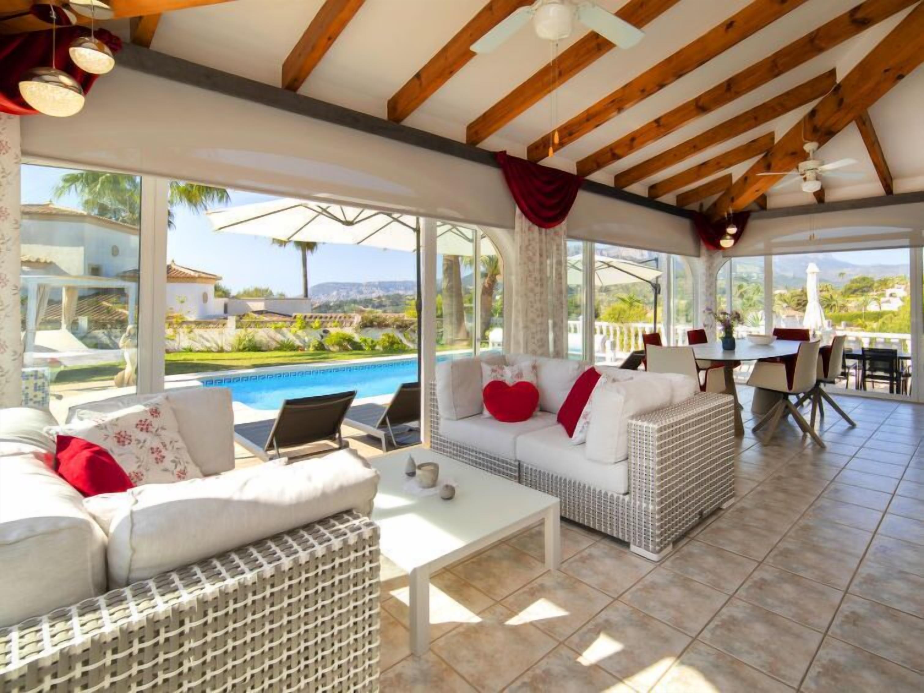 Un vaste espace de vie avec vue sur la piscine, des meubles en osier et un coin repas avec des sièges d’extérieur.