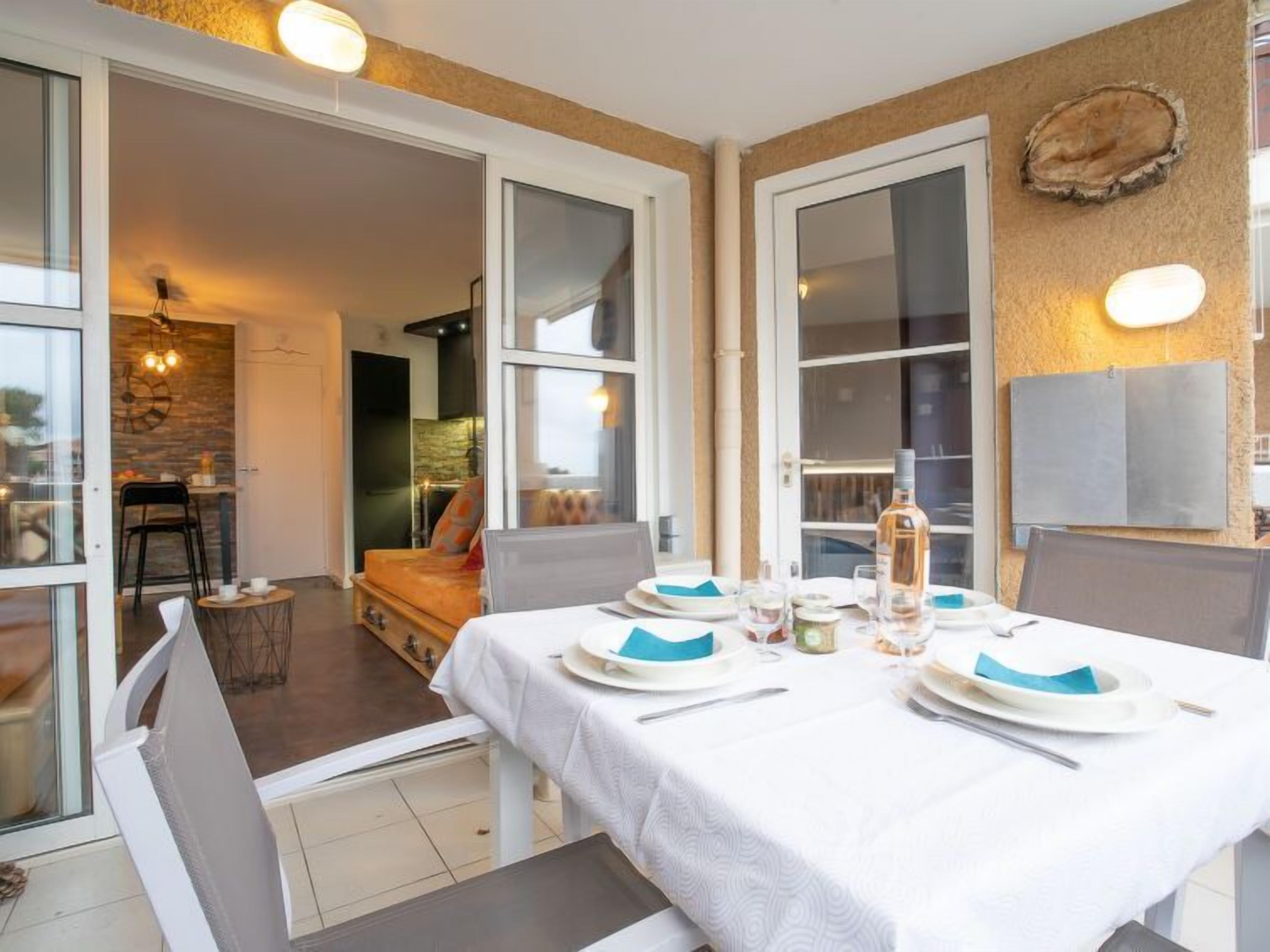 Un comedor con una mesa preparada para cuatro, un sofá y una silla visibles al fondo.
