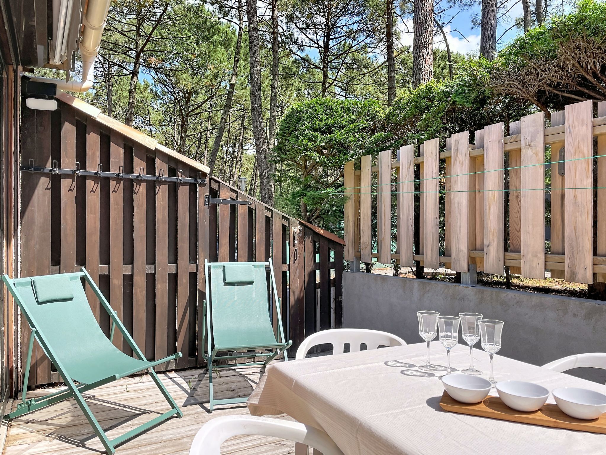 An outdoor patio with a table set for dining, two green chairs, and a wooden fence.