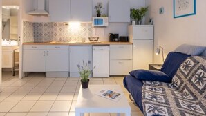 Een ruimtelijk ingedeelde leefruimte met kitchenette, een bank, een salontafel en een kleine eethoek.