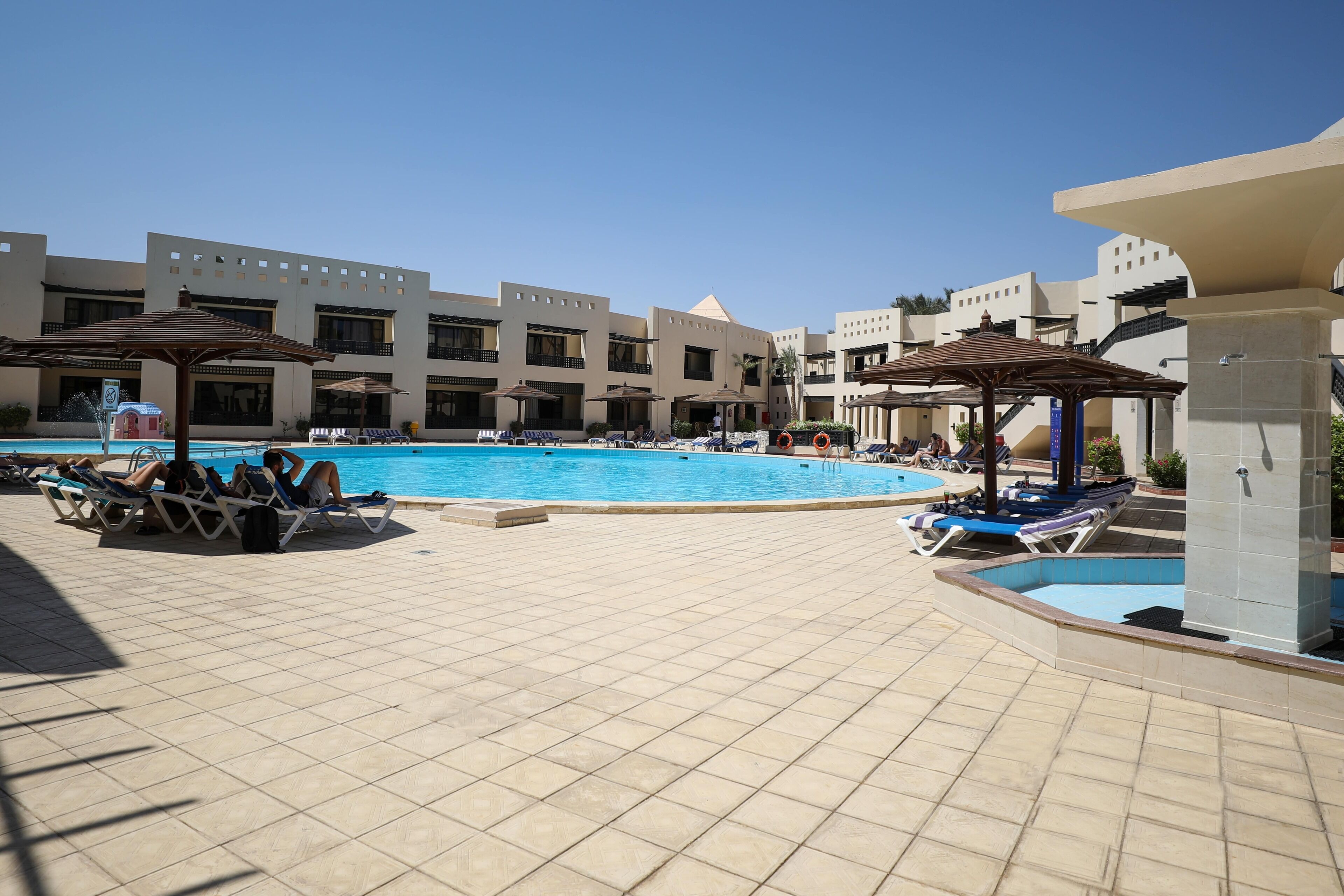 A pool area with sun loungers and umbrellas, surrounded by buildings with a modern architectural style.