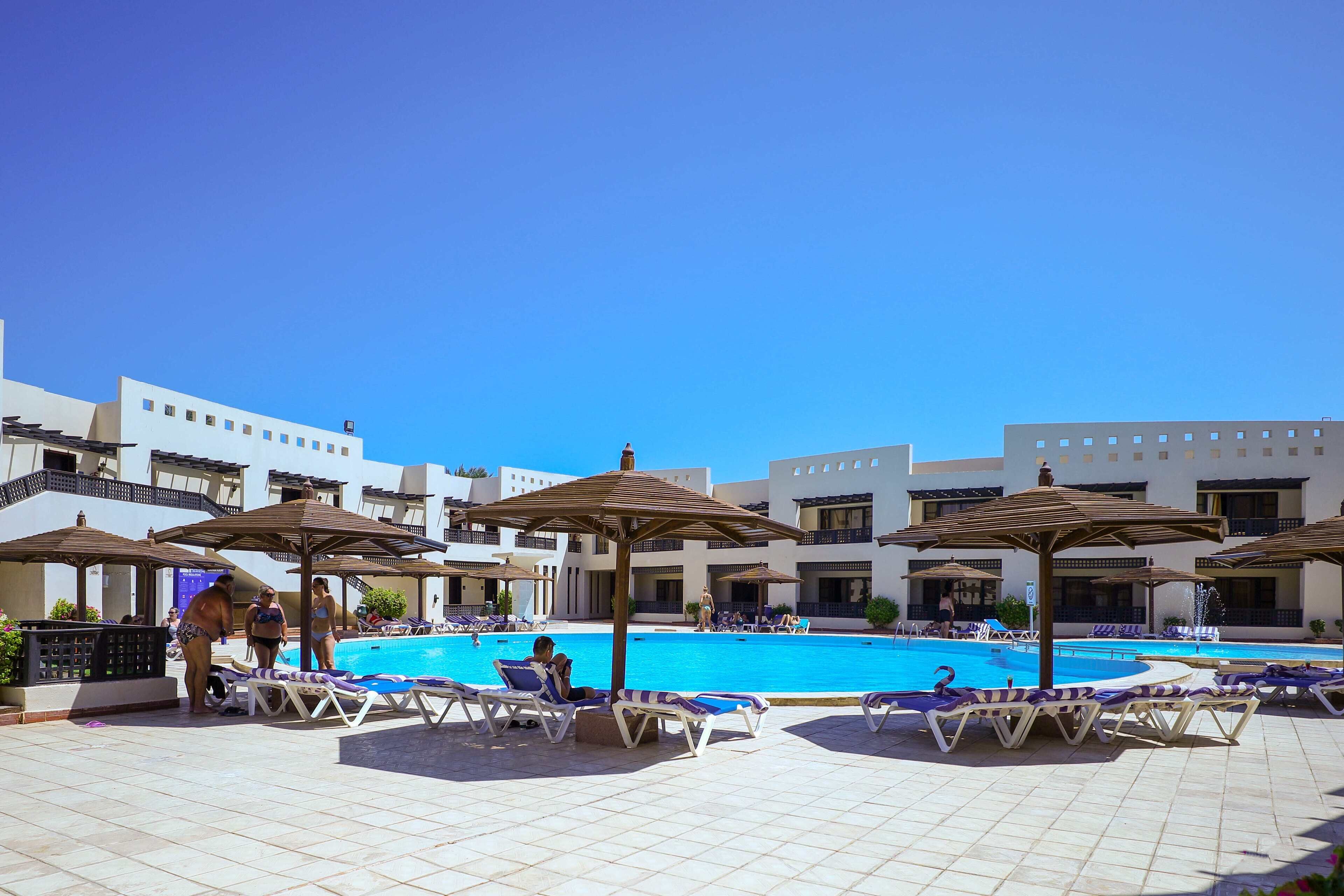 A poolside area with lounge chairs and umbrellas, a clear blue sky, and a pool.