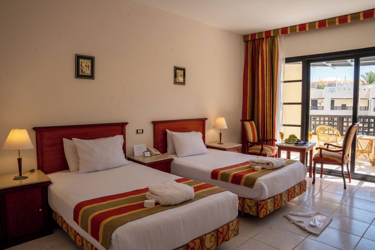 A hotel room with two beds, a balcony, and a view of buildings.