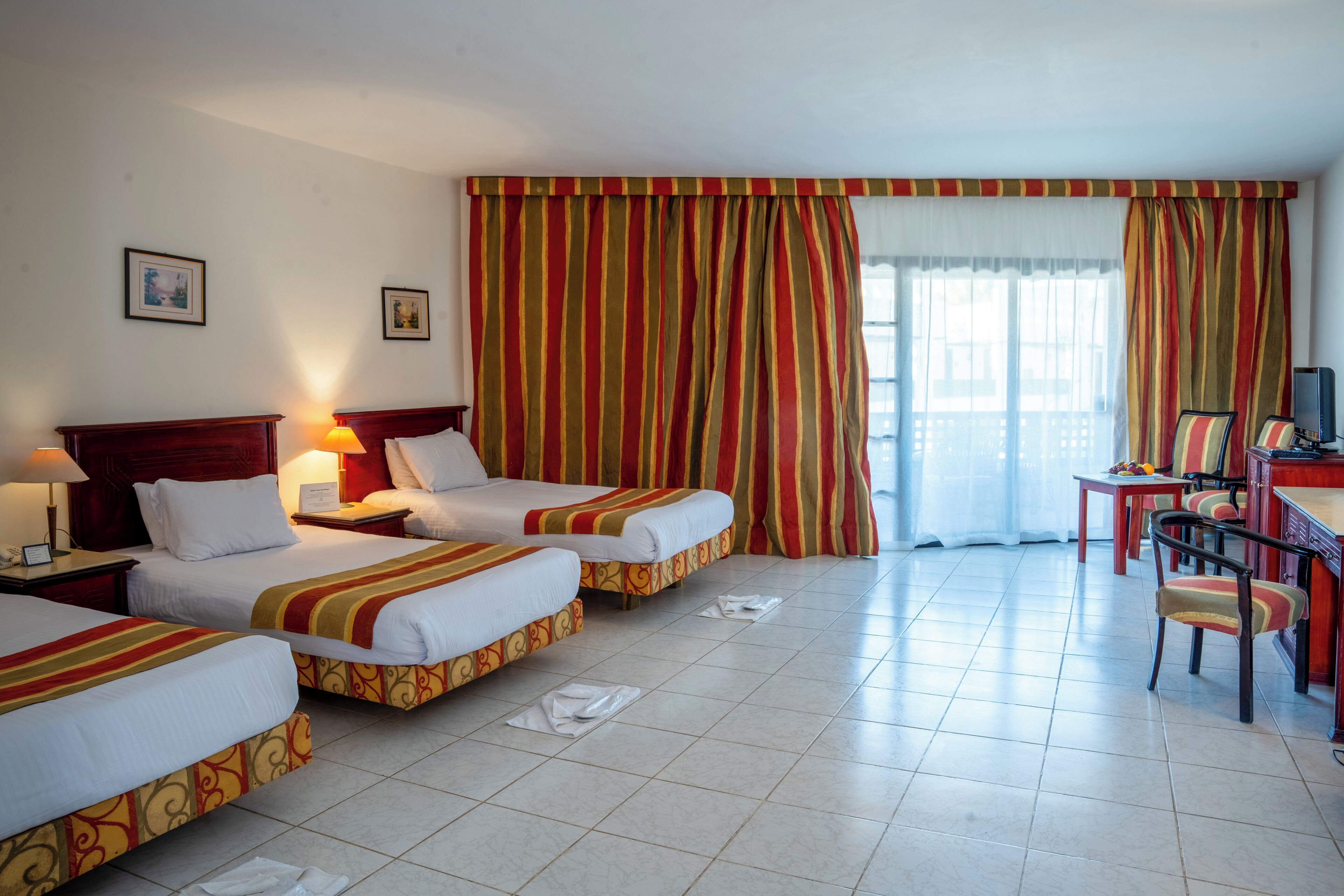 Une chambre d’hôtel avec deux lits, un bureau avec une chaise, une télévision et une grande fenêtre avec des rideaux.