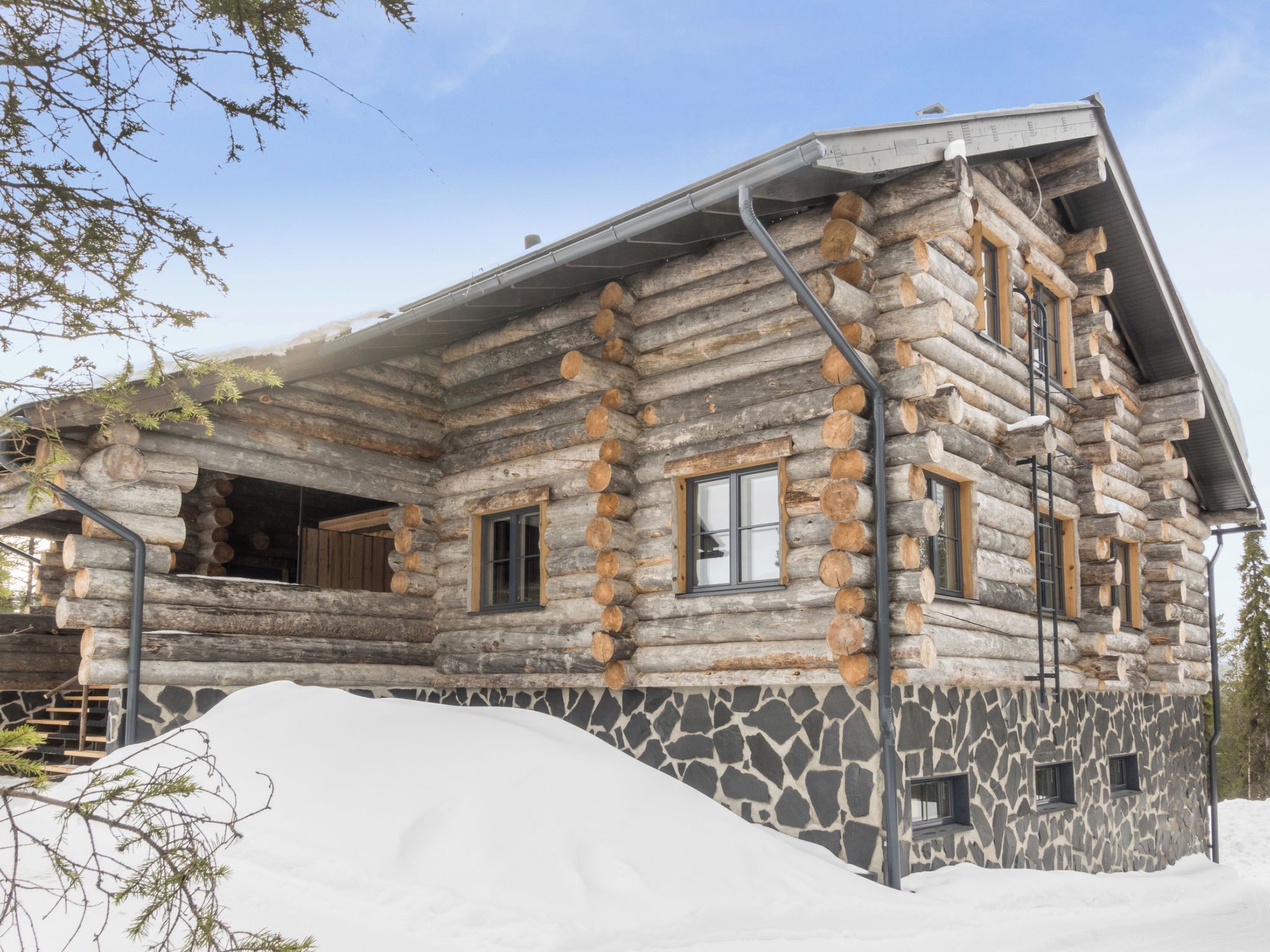 A log cabin with a stone foundation, multiple windows, and a snow-covered ground.