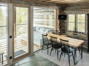 A rustic cabin interior with a wooden dining table, black chairs, a wicker sofa, and a stone fireplace.