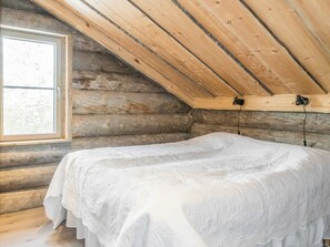 Una habitación tipo cabaña de madera con una cama, una ventana y techo inclinado.