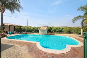 A swimming pool with a stone structure, surrounded by a brick patio and a fence.