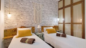 Une chambre d  ’hôtel avec deux lits, un mur en pierre, des têtes de lit en bois et une grande fenêtre.