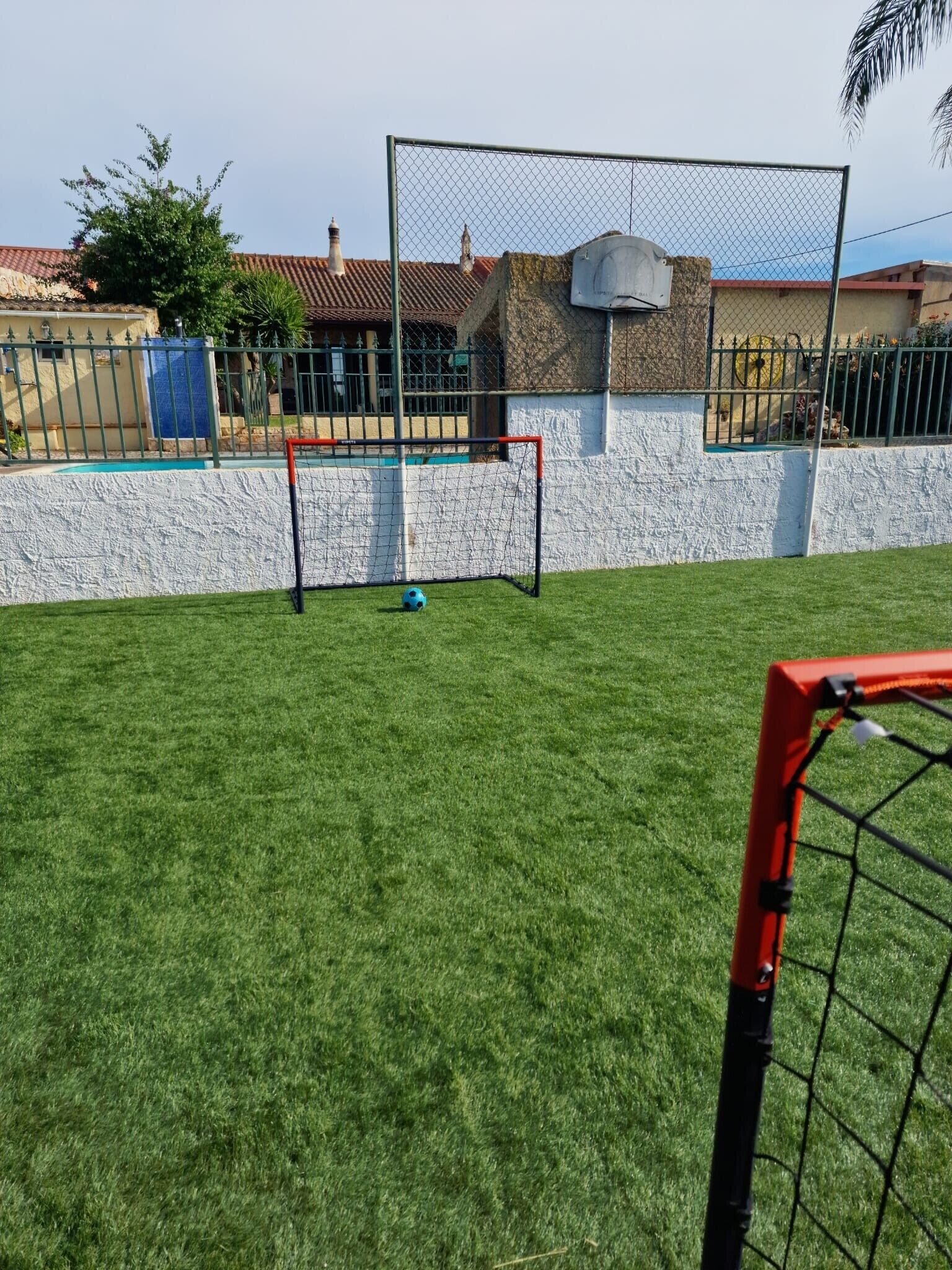 A fenced backyard with a goalpost, artificial grass, and a white wall.
