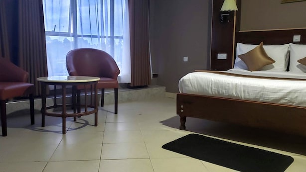 Quarto de hotel com cama, duas poltronas, uma mesa redonda pequena e vista pela janela.