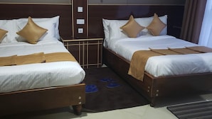 Duas camas lado a lado, com cabeceiras marrons, roupa de cama branca e almofadas marrons.