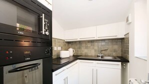 Een compacte keuken met een ingebouwde magnetron, oven en vaatwasser. De keuken heeft witte kastjes, een zwart aanrechtblad en een roestvrijstalen spoelbak.