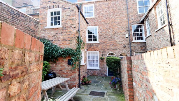 A courtyard with a stone floor, a wooden bench, and a brick wall with ivy. - Stodham House Quirky Central Townhouse, 4 beds sleeps up to 9 (York)