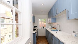 A narrow kitchen with blue cabinets, a white countertop, and a window overlooking a brick building. - Stodham House Quirky Central Townhouse, 4 beds sleeps up to 9 (York)