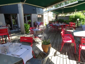 An outdoor dining area with tables and chairs, potted plants, and a covered section. - Logis Hotel de la Tour (Dunieres)