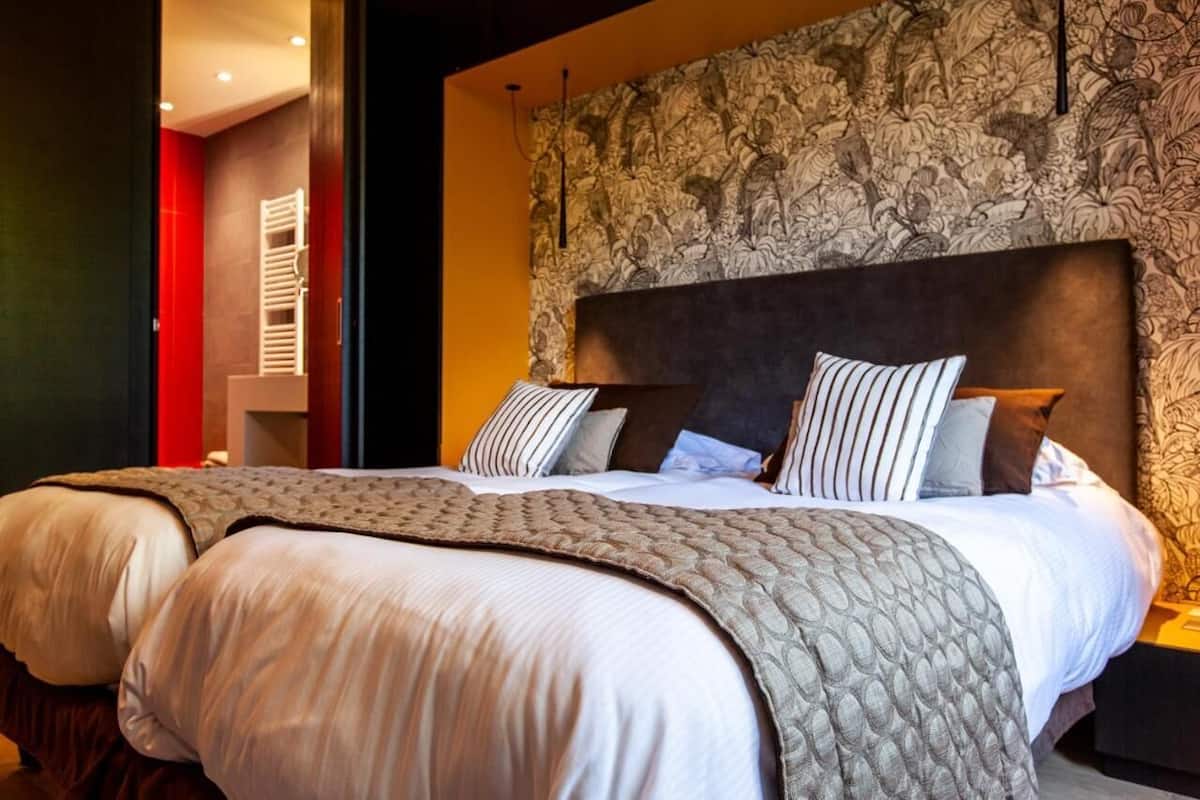 A hotel room with a large bed, a headboard with a floral pattern, and a red accent wall.