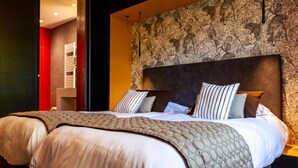 A hotel room with a large bed, a headboard with a floral pattern, and a red accent wall. - Logis Hotel de la Tour (Dunieres)