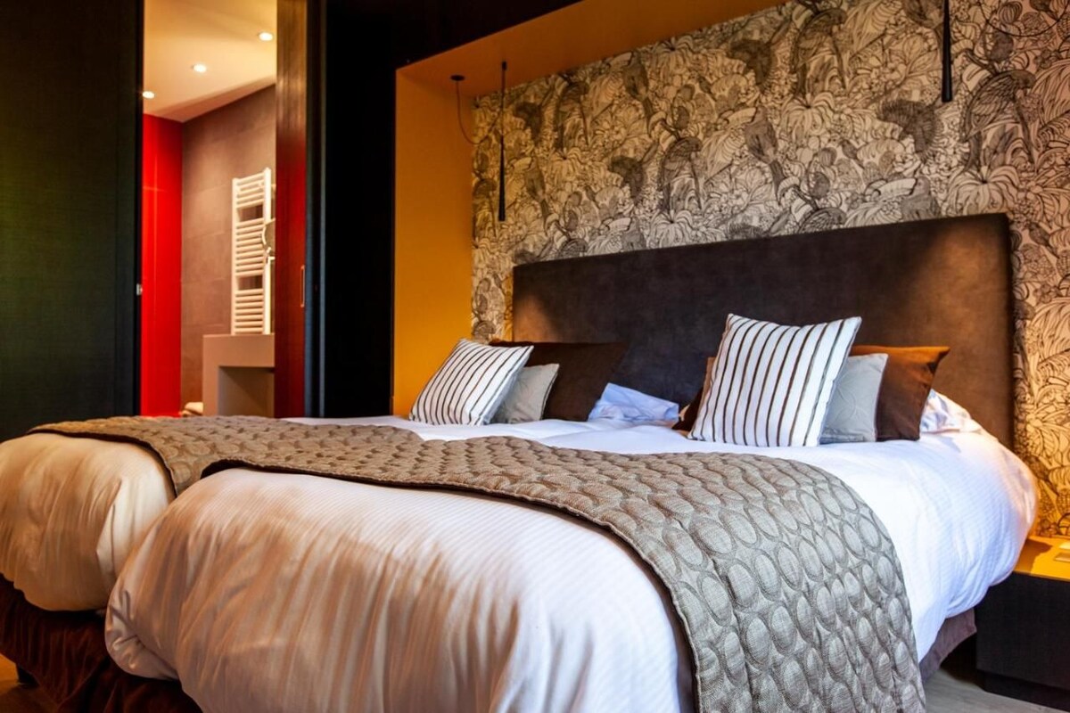 A hotel room with a large bed, a headboard with a floral pattern, and a red accent wall.
