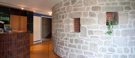 Un muro de piedra curvado con un ventanal pequeño y una planta. Se ve un mostrador de madera a la izquierda.