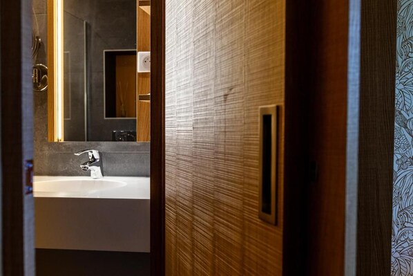 A bathroom with a modern sink, a mirror, and a wooden door. - Logis Hotel de la Tour (Dunieres)