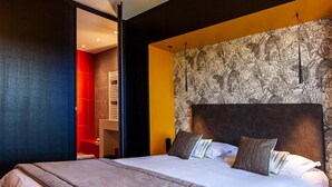 A modern hotel room with a large bed, a headboard with a patterned wallpaper, and a red accent wall. - Logis Hotel de la Tour (Dunieres)