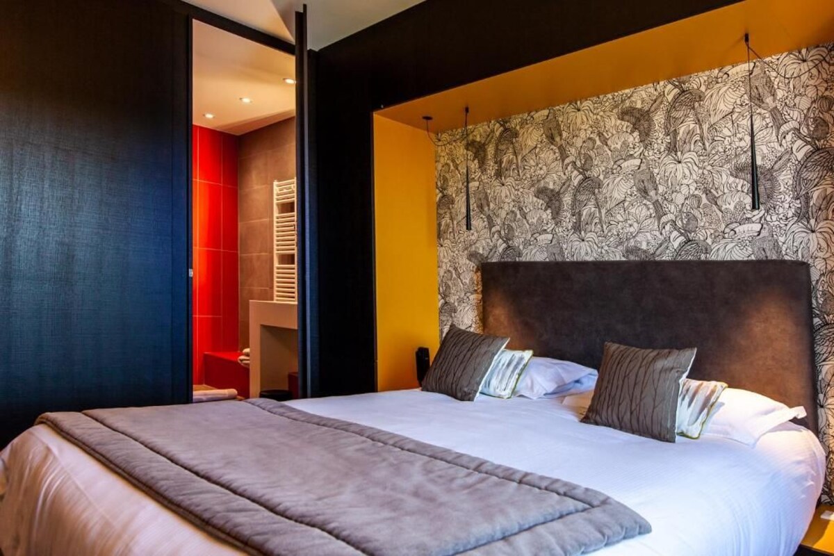 A modern hotel room with a large bed, a headboard with a patterned wallpaper, and a red accent wall.