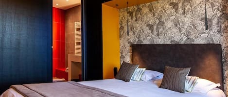 A modern hotel room with a large bed, a headboard with a patterned wallpaper, and a red accent wall.
