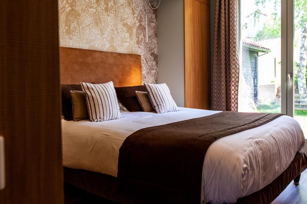 A neatly made bed with striped pillows, a brown headboard, and a view of greenery outside.