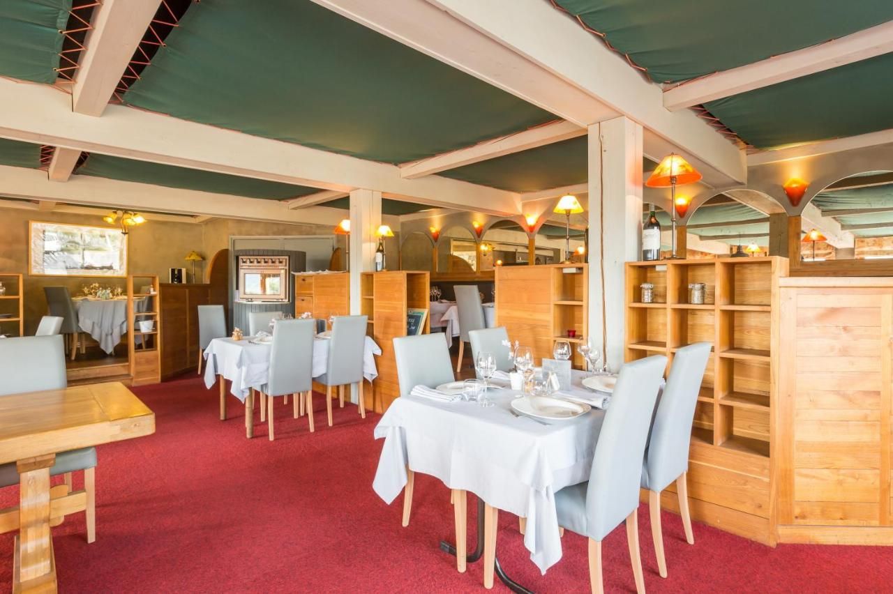 A restaurant with wooden furniture, tables set with white tablecloths, and a red carpeted floor.