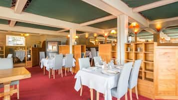 A restaurant with wooden furniture, tables set with white tablecloths, and a red carpeted floor.