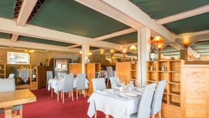 Un restaurante con muebles de madera, mesas dispuestas con manteles blancos y un piso cubierto de alfombra roja.