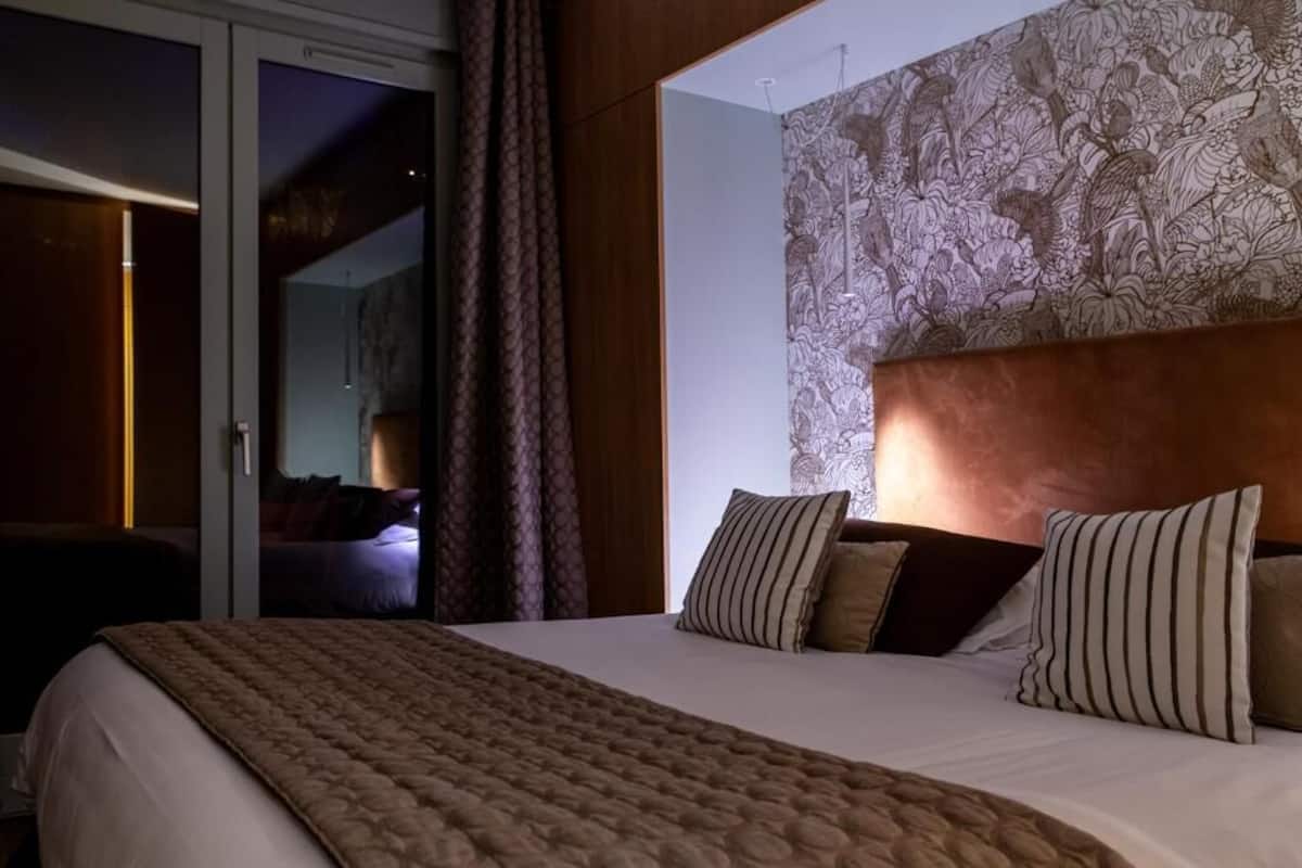 A hotel room with a large bed, a patterned headboard, and a view through a sliding door.