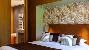 A hotel room with a large bed, a wooden headboard, and a wall with a floral tapestry. - Logis Hotel de la Tour (Dunieres)