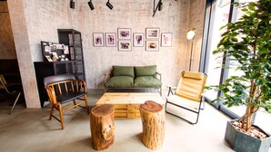 A cozy room with a wooden bench, a green sofa, and a wooden coffee table. There are framed pictures on the wall and a potted plant. - Ten to Ten Hostel (Sapporo)