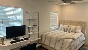 Un dormitorio con cama, escritorio con computadora, estantes y ventilador de techo.