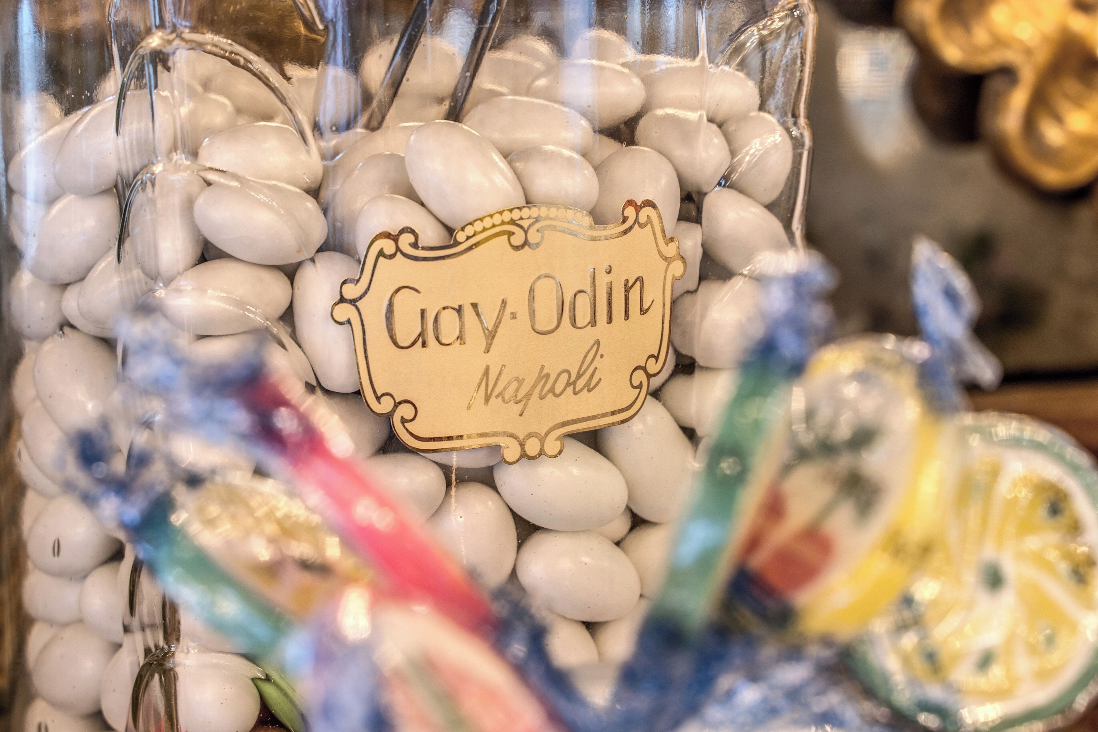 Un recipiente de vidrio lleno de caramelos blancos etiquetados como 'Gay-Odin Napoli'.