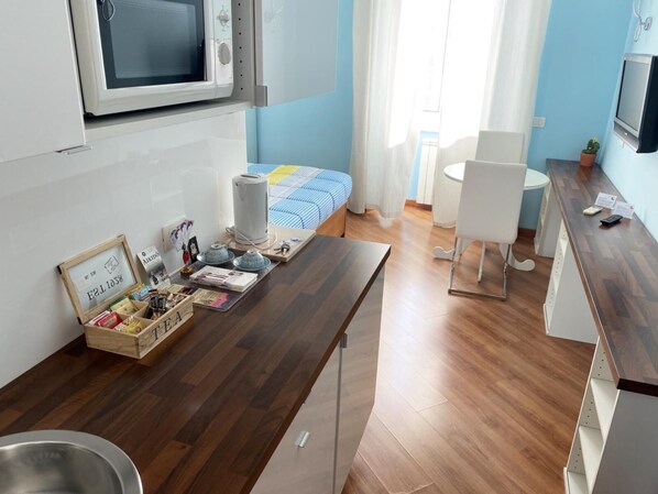 Cocina compacta con microondas, hervidor y una pequeña mesa de comedor con juego de té.