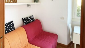 A room with a pink and orange sofa, a white table, and a wall-mounted shelf with decorative items.