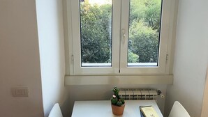 A small, white table with a potted plant and a book, positioned under a window with a view of greenery outside.