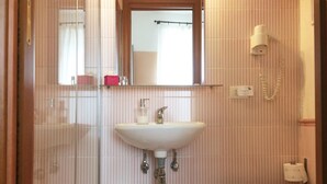 Une salle de bain avec une douche à parois de verre, un lavabo blanc avec un miroir au-dessus, des toilettes et une poubelle.