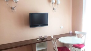 Une pièce dotée d’un téléviseur à écran plat fixé au mur, d’une petite table avec des chaises et de deux lampes murales.