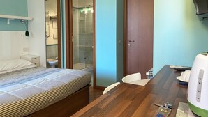 A hotel room with a bed, a wooden dining table, a chair, a white kettle, and a door leading to a bathroom. - Luna Rossa Guest House   Green Double room with garden view (ROMA)