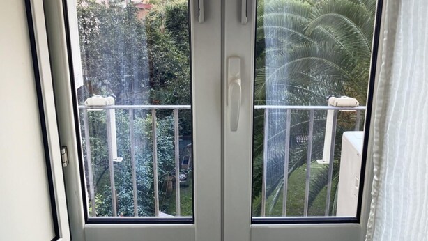 A balcony with a metal railing, a white door, and a view of a residential area with trees and buildings. - Luna Rossa Guest House   Green Double room with garden view (ROMA)