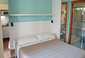 Un dormitorio con cama, mesitas de noche, una lámpara verde colgante y vistas a un baño con inodoro y lavabo.